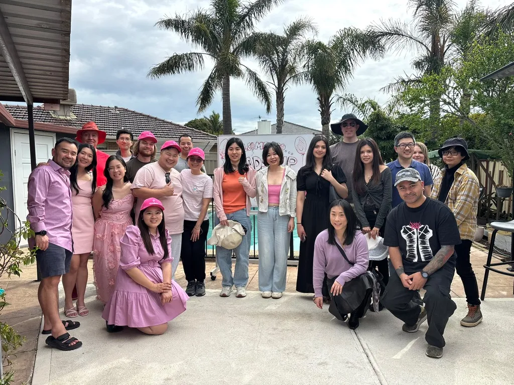 About twenty friends gathered in a sunny backyard for the HeadsUp launch party, many in pink and several in pink HeadsUp caps, in front of a hand-drawn welcome sign
